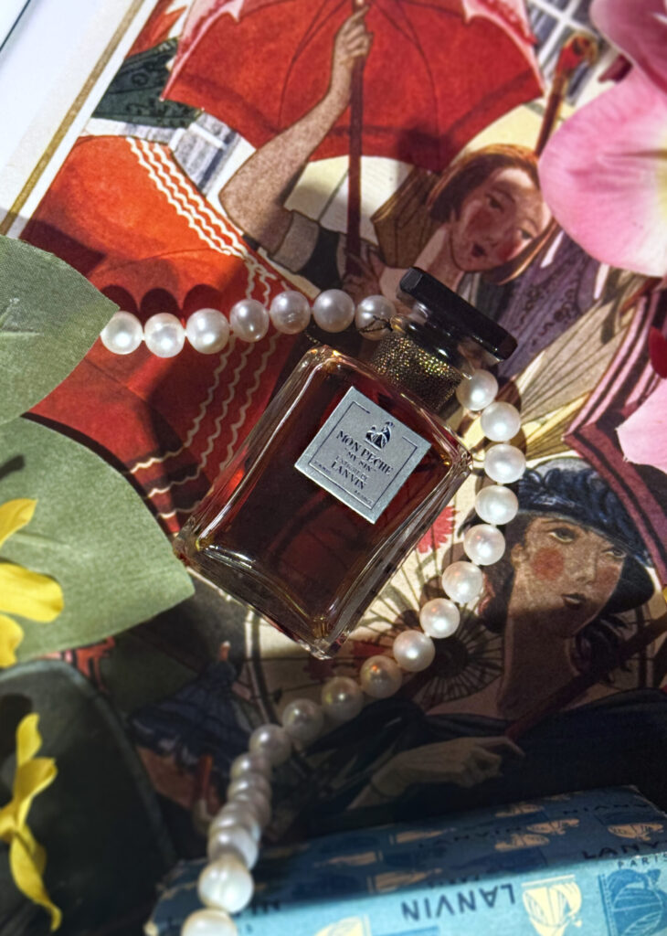 Extrait bottle of Lanvin Mon Peche (My Sin), surrounded by flowers and pearls, over an illustration of women with parasols.