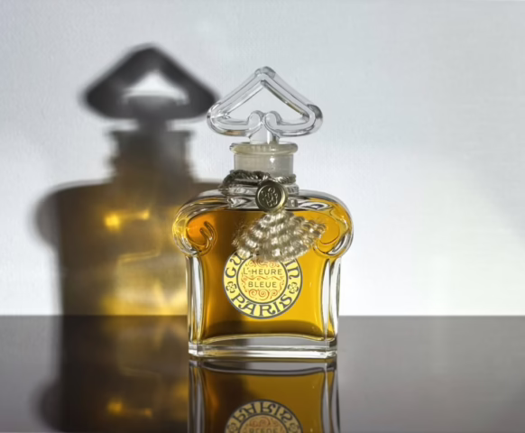A bottle of Guerlain's L'Heure Bleue against a white background on top of a black reflective surface